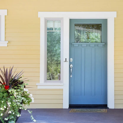 Silver whale tail-shaped object on a white doorframe with blue door on a yellow house